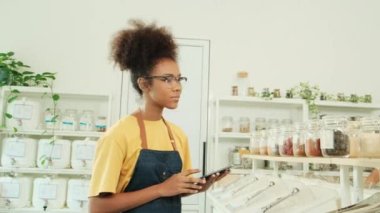 Siyahi kadın esnaf, perakende satış mağazasındaki doğal organik ürünlerin stoklarını kontrol ediyor. Sıfır atık ve plastiksiz bakkal, çevre dostu, sürdürülebilir yaşam tarzları, yeniden kullanılabilir konteynırlar..