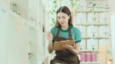 Beyaz kadın esnaf, perakende satış mağazasındaki doğal organik ürünlerin stoklarını kontrol ediyor. Sıfır atık ve plastiksiz bakkal, çevre dostu, sürdürülebilir yaşam tarzları, yeniden kullanılabilir konteynırlar..