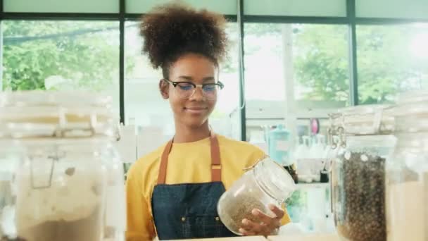 一位年轻的黑人女店主在一家再装配店 零废物商店 一家无塑料杂货店和一家环保零售商店里 用可重复使用的容器清洁玻璃瓶中的天然有机产品 — 图库视频影像