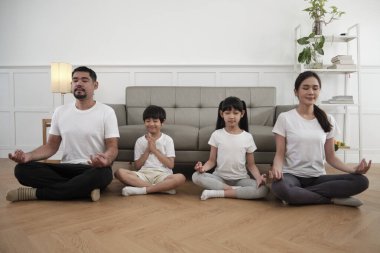 Mutlu Asya Taylandlı aileler, aileler ve çocuklar oturma odasında birlikte oturur, gözlerini kapatır, lotus pozisyonunda huzur içinde meditasyon yapar, ve sağlıklı yoga yapar, ev yaşamını sürdürür..