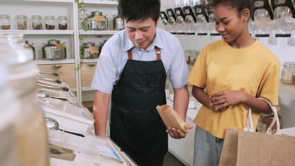 零售商店的服务人员 亚洲男性店主用回收的纸袋 零废品杂货 有机产品 可持续的生活方式 在补货商店向顾客兜售零食 — 图库视频影像