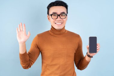 Asyalı adam mavi arka planda akıllı telefon kullanıyor