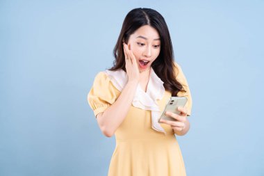 Güzel genç Asyalı kadın mavi arka planda akıllı telefon kullanıyor.