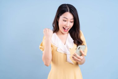 Güzel genç Asyalı kadın mavi arka planda akıllı telefon kullanıyor.