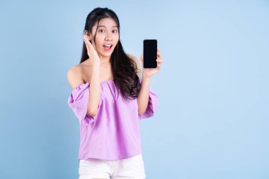 Genç Asyalı kız mavi arka planda akıllı telefon kullanıyor.