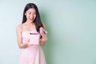 Güzel genç Asyalı kadın yeşil arka planda pembe hediye kutusu tutuyor.