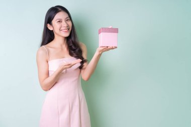 Güzel genç Asyalı kadın yeşil arka planda pembe hediye kutusu tutuyor.