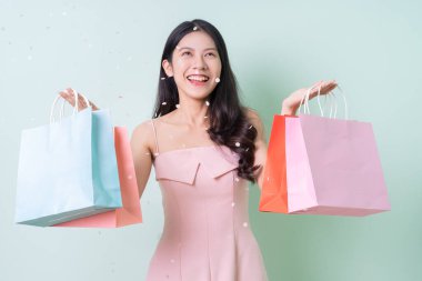 Yeşil arka planda alışveriş torbası tutan güzel bir Asyalı kadın.