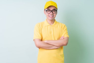 Genç Asyalı teslimatçı yeşil arka planda poz veriyor.