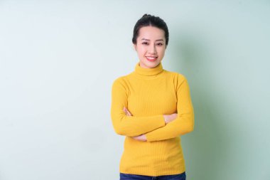 Yeşil arka planda süveter giyen güzel bir Asyalı kadın.