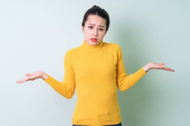 Yeşil arka planda süveter giyen güzel bir Asyalı kadın.