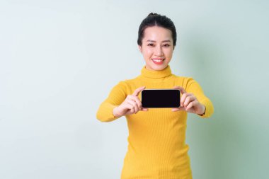 Yeşil arka planda süveter giyen güzel bir Asyalı kadın.