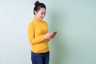 Yeşil arka planda süveter giyen güzel bir Asyalı kadın.