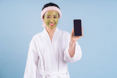 Mavi arka planda bornoz giyen genç Asyalı kadın.