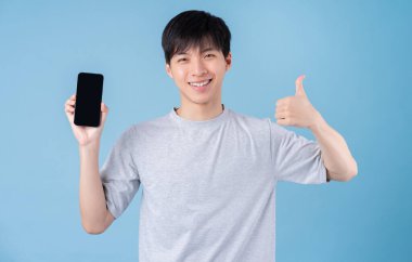 Genç Asyalı adam mavi arka planda akıllı telefon kullanıyor.