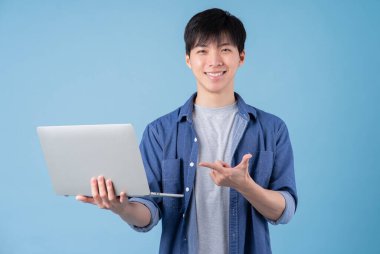 Genç Asyalı adam mavi arka planda dizüstü bilgisayar kullanıyor