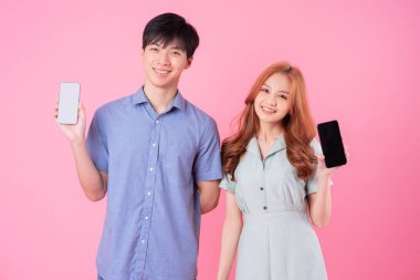 Genç Asyalı çift pembe arka planda akıllı telefon kullanıyor.