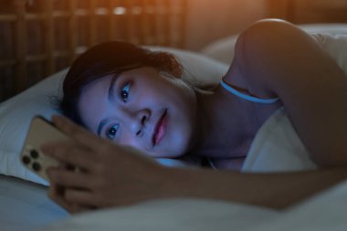 Güzel genç Asyalı kadın yatmaya hazırlanırken akıllı telefon kullanıyor.