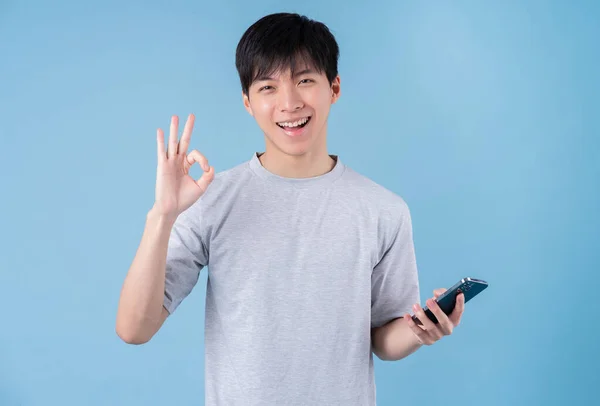 青の背景にスマートフォンを使う若いアジア人男性 — ストック写真