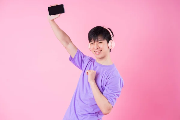 若いアジア人男性リスニング音楽上のピンクの背景 — ストック写真