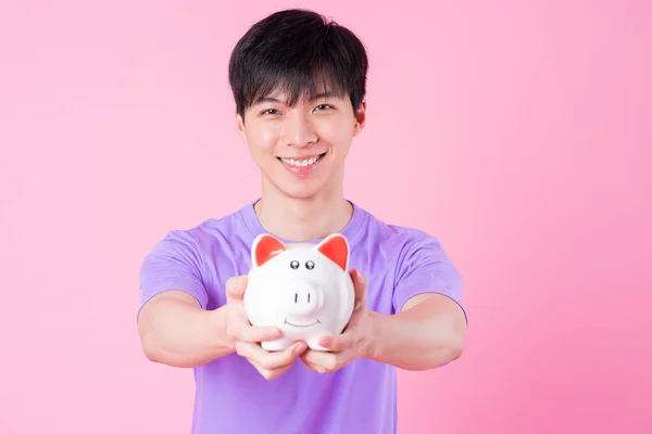 Jovem Ásia Homem Segurando Porquinho Banco Rosa Fundo — Fotografia de Stock