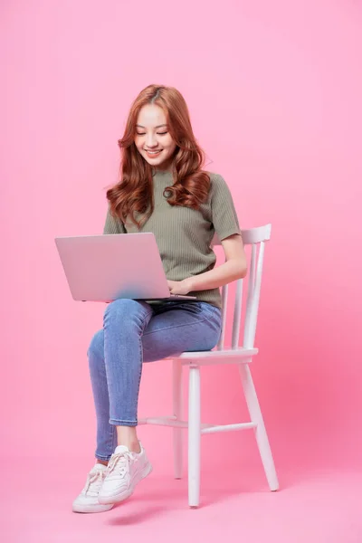 아시아 소녀가 분홍색 배경에 앉아서 랩탑을 사용하는 — 스톡 사진