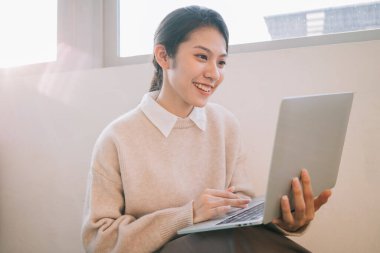 Genç Asyalı iş kadını evde dizüstü bilgisayar kullanıyor.