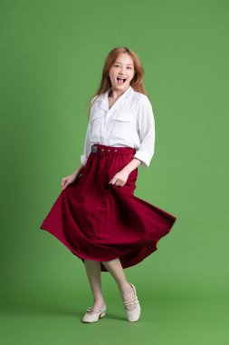 Güzel genç Asyalı kadın dans ediyor ve yeşil arka planda poz veriyor.