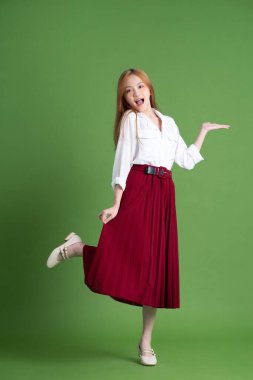 Güzel genç Asyalı kadın dans ediyor ve yeşil arka planda poz veriyor.