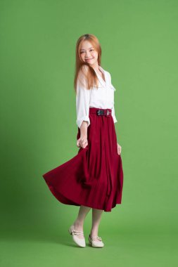 Güzel genç Asyalı kadın dans ediyor ve yeşil arka planda poz veriyor.