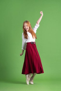 Güzel genç Asyalı kadın dans ediyor ve yeşil arka planda poz veriyor.