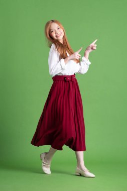 Güzel genç Asyalı kadın dans ediyor ve yeşil arka planda poz veriyor.