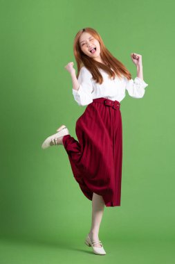 Güzel genç Asyalı kadın dans ediyor ve yeşil arka planda poz veriyor.