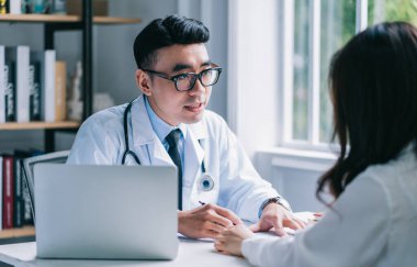 Asyalı erkek doktor klinikteki hastayı muayene ediyor.