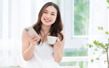 Genç Asyalı kadın sabah evde akıllı telefon kullanıyor.