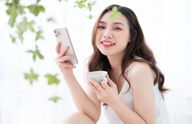 Genç Asyalı kadın sabah evde akıllı telefon kullanıyor.