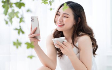 Genç Asyalı kadın sabah evde akıllı telefon kullanıyor.