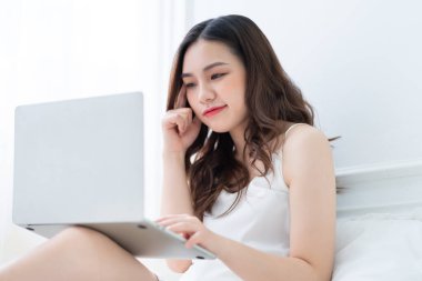 Genç Asyalı kadın yatakta dizüstü kullanarak