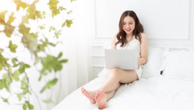 Genç Asyalı kadın yatakta dizüstü kullanarak