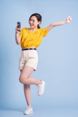 Mavi arka planda akıllı telefon kullanan genç Asyalı kadının tam boy görüntüsü