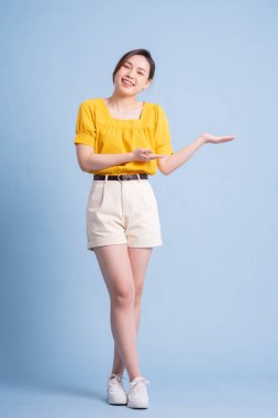 Mavi arka planda poz veren genç Asyalı kadının tam boy görüntüsü