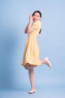 Güzel genç Asyalı kadın mavi arka planda dans ediyor.