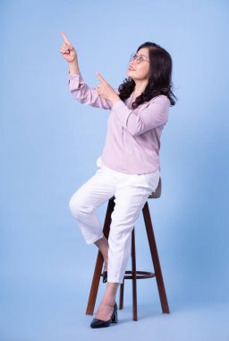 Mavi arka planda orta yaşlı Asyalı kadının tam boy resmi