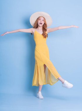 Mavi arka planda sarı elbise giyen genç Asyalı kadının tam boy görüntüsü.