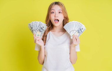 Sarı arka planda para tutan Asyalı genç bir kız resmi