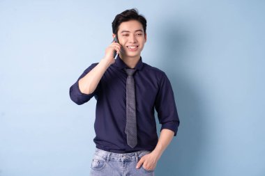 Portrait of young Asian businessman using smartphone on blue background