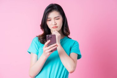 Genç Asyalı kadın pembe arka planda akıllı telefon kullanıyor.