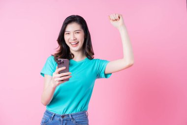 Genç Asyalı kadın pembe arka planda akıllı telefon kullanıyor.