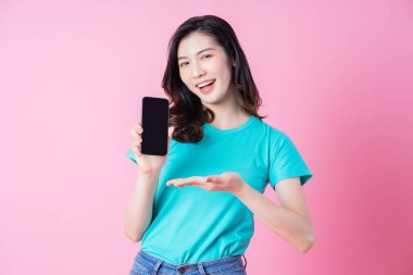 Genç Asyalı kadın pembe arka planda akıllı telefon kullanıyor.