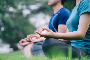 Genç Asyalı bir çiftin çimlerin üzerinde birlikte meditasyon yapması.